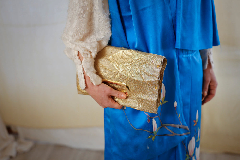 A clutch of gold woven fabric beside the painted branches of the dress.