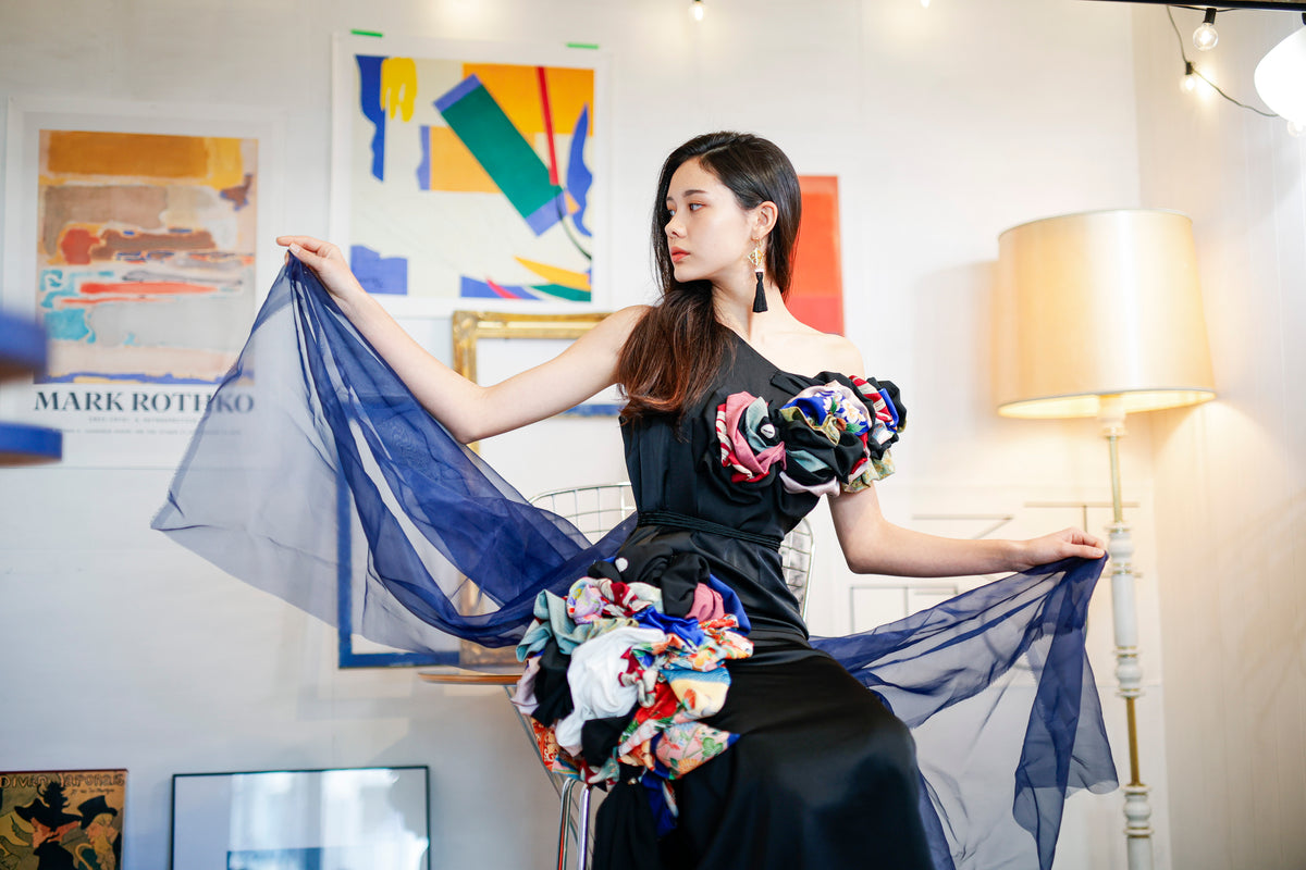 Kimono-fabric frills sit at the shoulder and waist of a black dress. Both hands spread the navy tulle.