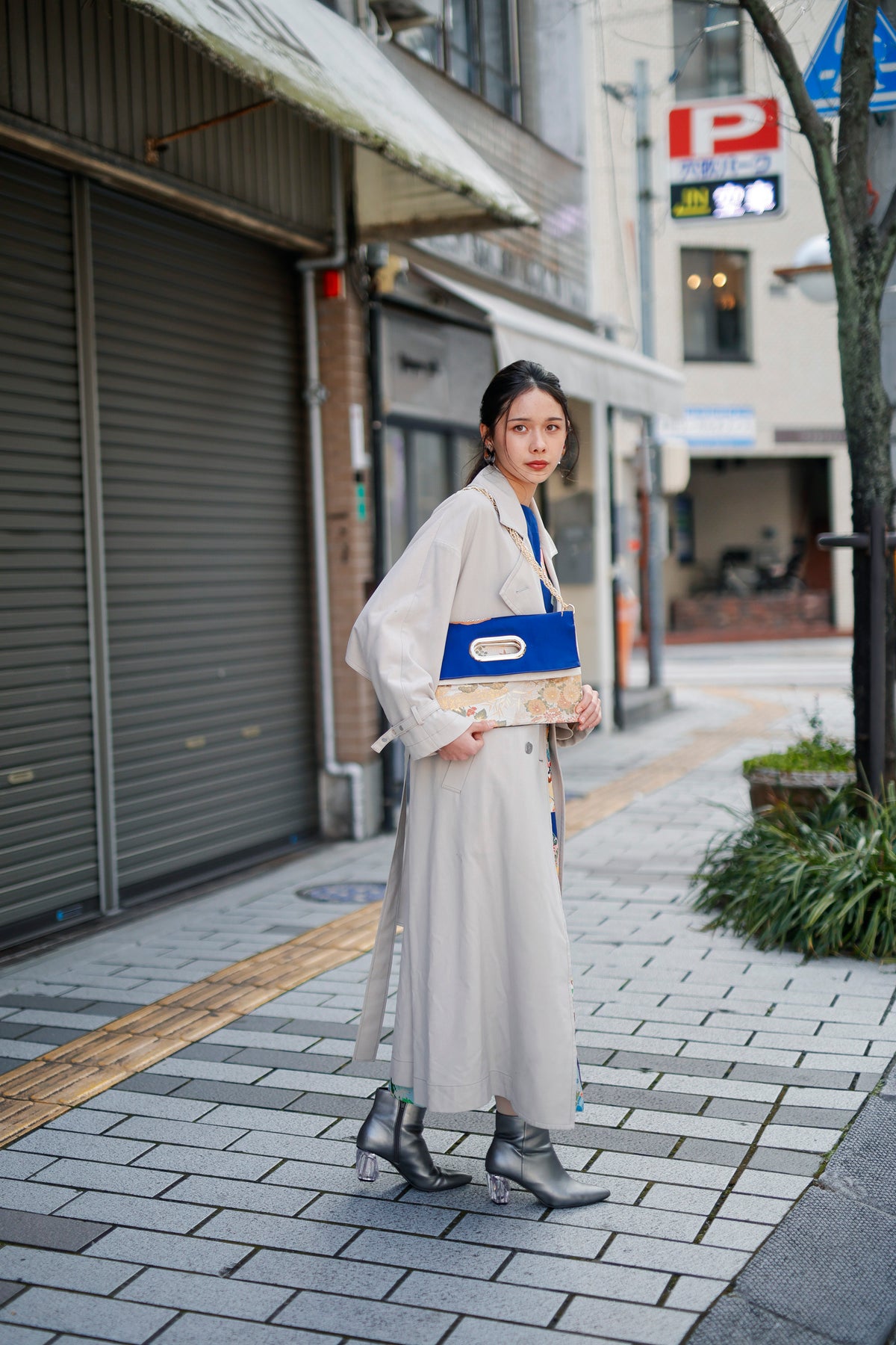 In a shopping street, a blue and ivory obi-fabric bag hangs from the shoulder. Kimono fabric from the dress shows at the hem.