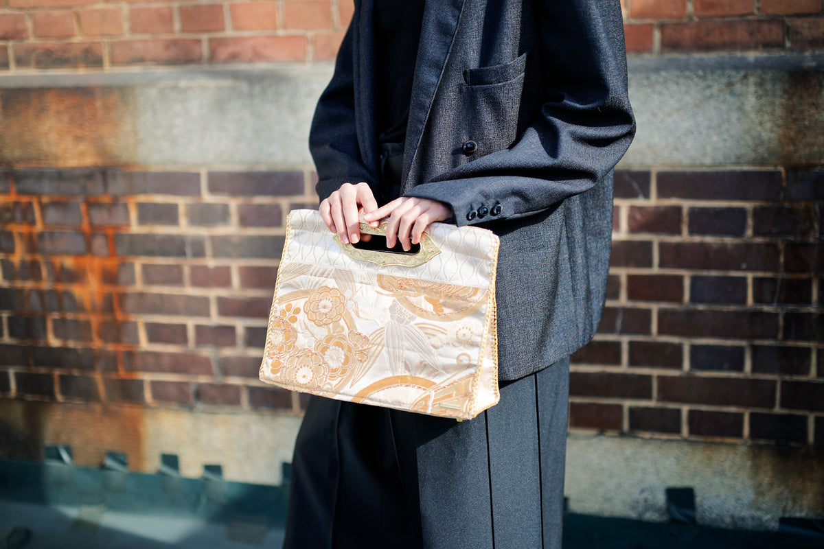 Both hands hold a MIKOSHI Bag in ivory and gold obi.