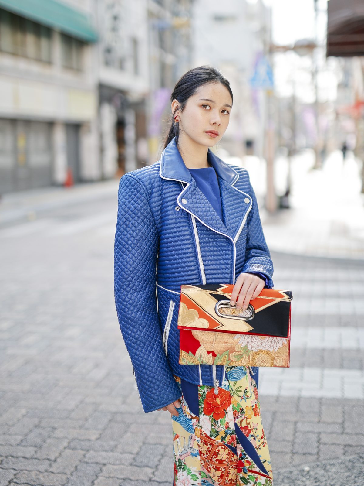 赤と黒に金の OBI Bag。折りたたんで片手で持ち、商店街に立つ